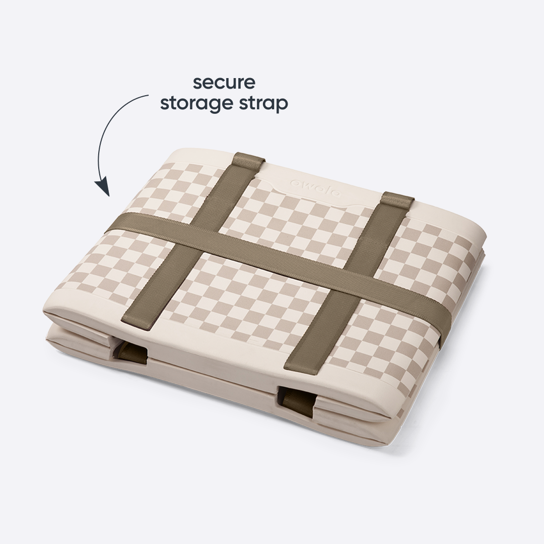 Owala Sun-Day Collapsible Tote in Checkin' In shown folded flat with its storage strap secured across the top, cream and tan checker exterior with olive green storage strap, with text overlay reading "storage strap"